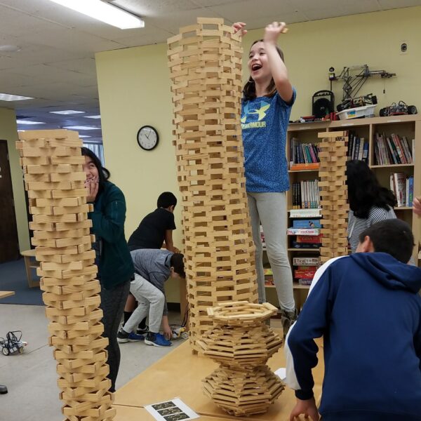 A smiling girl building a large Kapla Tower.